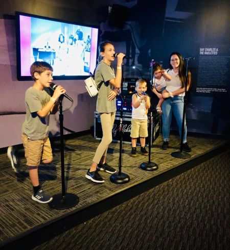 Three kids Maryssa, Kaiser and Jace singing on a stage where Jenelle  is on the side carrying two-year-old daughter Ensley.